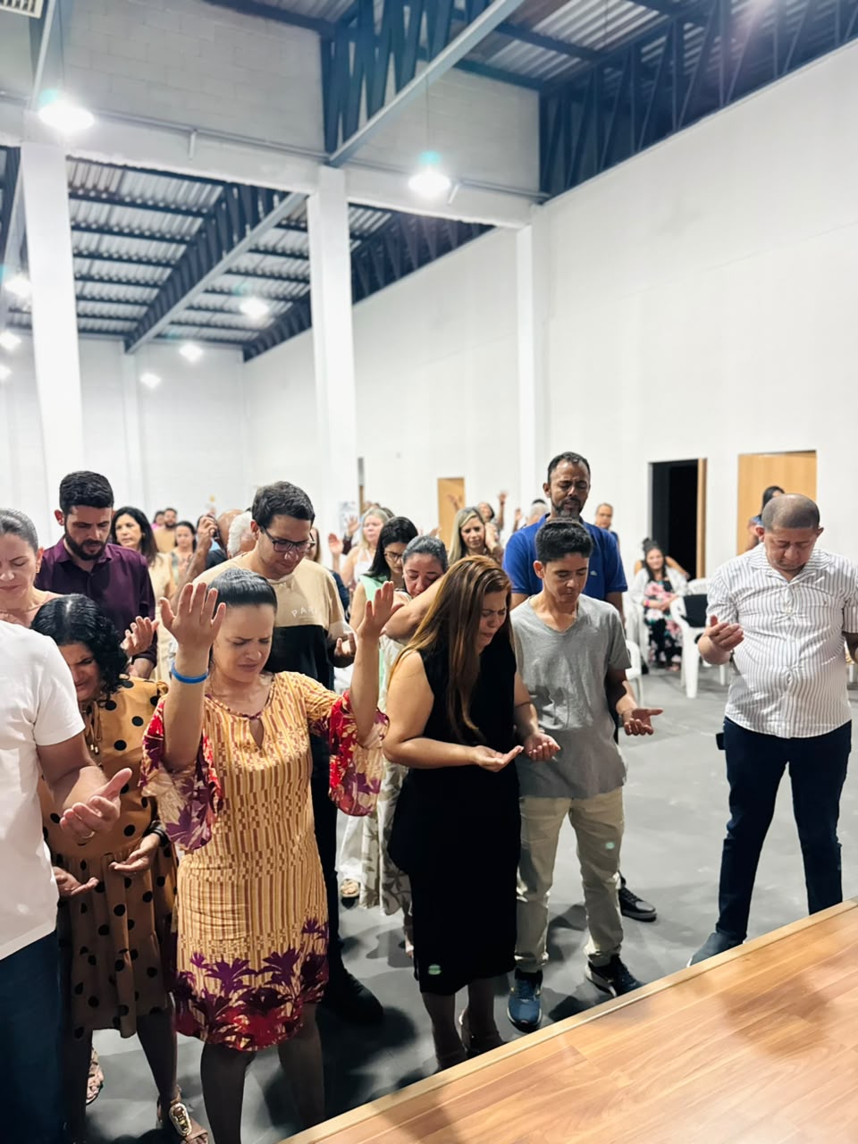 Grupo de irmãos em pé, orando juntos com as mãos e os corações abertos.
